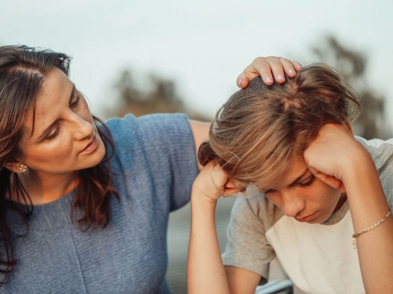 Mama pociesza zasmuconego nastolatka siedzącego z opuszczoną głową